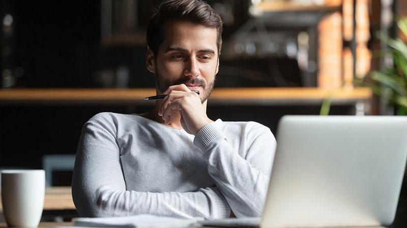 Adult male at desk with open laptop and pen